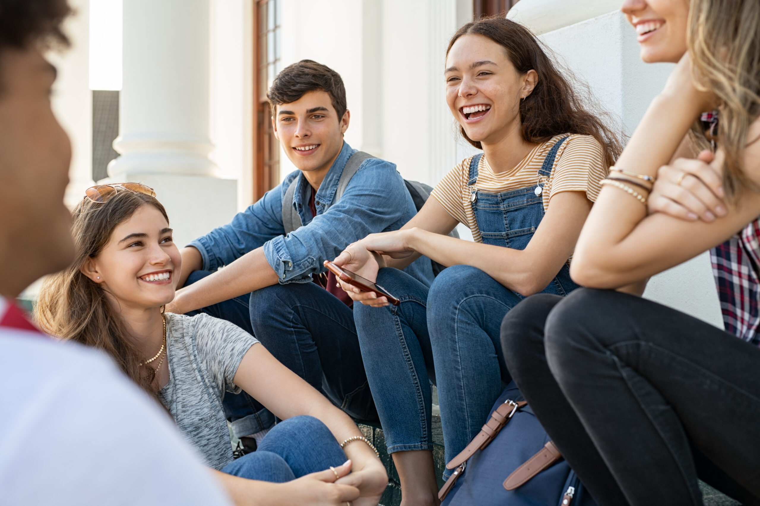 Group of international teenagers sitting on steps, smiling and talking together during a Residential English Camp.