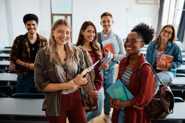 Smiling international students holding books in a classroom, preparing for IELTS exam practice with a focus on reading, writing, listening, and speaking to build confidence and achieve higher scores.