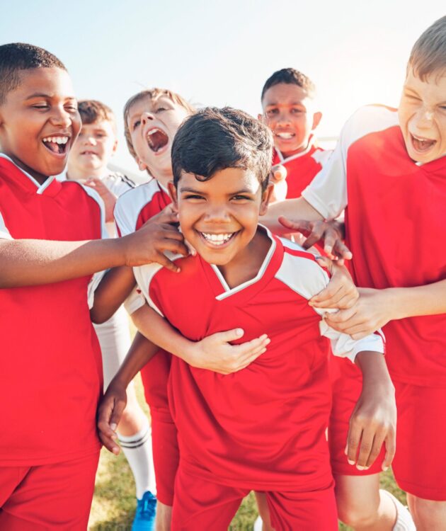 Children in red football kits smiling and playing together at a Residential English Camp in Hua Hin, part of the Premier Skills English British Council-inspired programme.